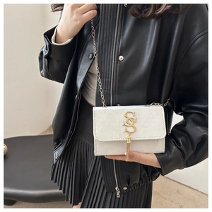 Detail of white mini crossbody bag featuring golden letter S hardware and fringe tassel
