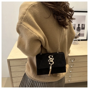 Detail of black crossbody bag with gold S-buckle and chain strap on female model
