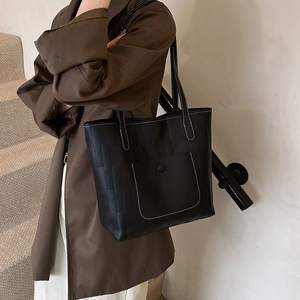 Black textured tote bag with white contrast stitching and front pocket on model