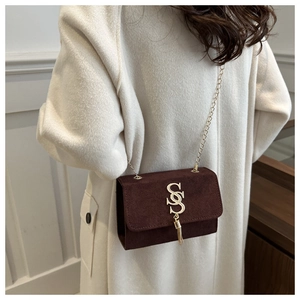 Brown suede crossbody bag with gold chain strap shown on model in long white coat