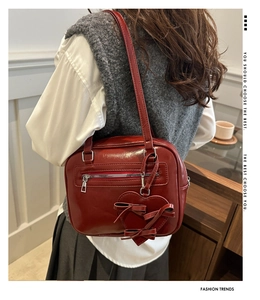 Detail of a dark red glossy shoulder bag with heart pendant and bow decoration