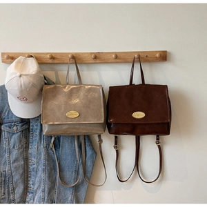 Detail of vintage oil-wax leather backpacks in taupe and dark brown with gold metal logo