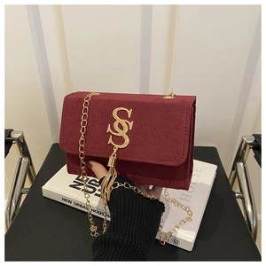 Detail of burgundy suede square bag featuring gold hollow logo and tassel chain strap