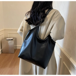 Minimalist large black tote bag with wide shoulder strap shown on a model in a studio