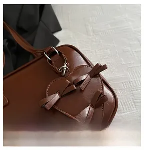 Detail view of dark brown glossy leather bag featuring heart patch and bow accents