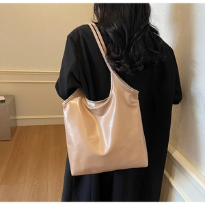 Large capacity beige tote bag in glossy PU leather worn over the shoulder for commute