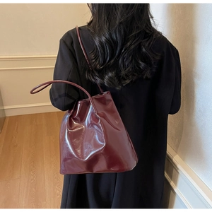 Detailed back view of a burgundy glossy patent leather tote bag worn by a female model