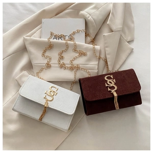 Close-up of suede crossbody bag with gold S-logo hardware and elegant metal chain tassel
