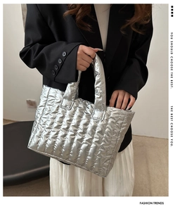 Detail of silver quilted tote bag with vertical stitching held by a model in a suit