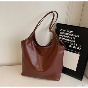 Detail of a large brown faux leather tote bag with smooth texture on a white surface