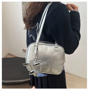 Silver shoulder bag with heart pendant and bow details shown on a female model
