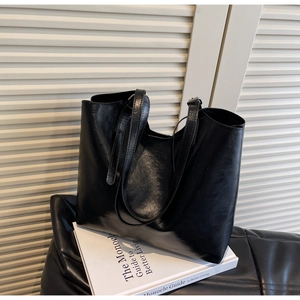 Detail of glossy black wax leather tote bag with long straps on a white book