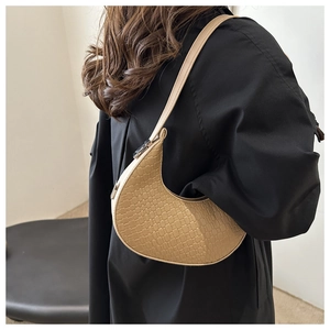 Détail du sac croissant beige à motif crocodile sur fond de manteau noir élégant