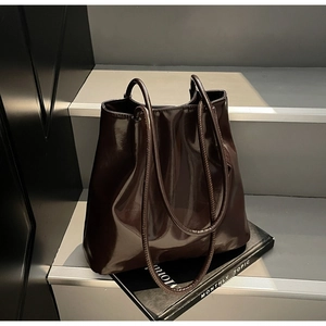 Macro detail of dark brown glossy patent leather shoulder tote bag on minimal stairs