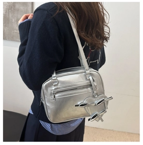 Detail of silver metallic crossbody bag with heart charm and bow decor on model