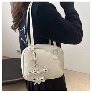 Detail view of heart pendant and bow charm on a minimalist cream white shoulder bag