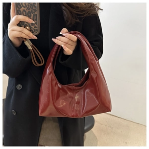 Détail du sac hobo en cuir verni rouge foncé porté avec un manteau en laine noir