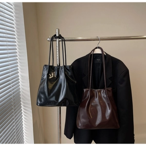 Detail of high-gloss glossy shoulder bags in black and dark brown on a metal hanger