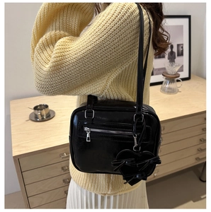 Detail of black glossy shoulder bag with silver hardware and heart bow charm on sweater