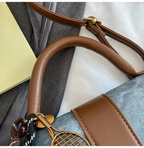Detail of denim crossbody bag with brown leather trim and golden tennis racket pendant