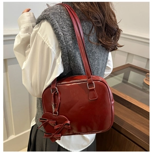 Detailed view of a dark red PU leather shoulder bag with heart bow charm on a model
