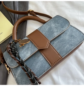 Close-up of blue denim and brown leather patchwork bag with woven tassel detail