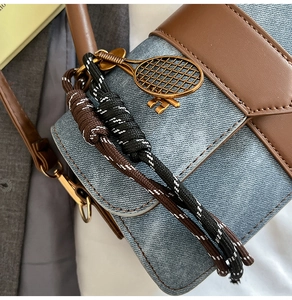 Detail of denim and brown leather stitching bag with a gold tennis racket pendant charm
