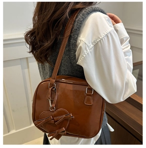 Detailed view of a vintage brown glossy shoulder bag with a heart bow pendant