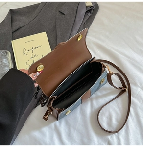 Detail of denim crossbody bag with brown leather trim and golden magnetic snap closure