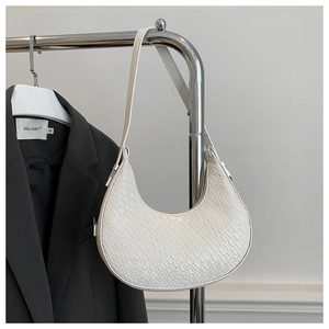 Gros plan sur un sac croissant blanc à motif crocodile suspendu sur un cintre