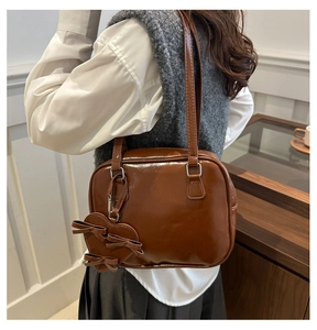 Brown patent leather shoulder bag with heart bow charm shown on model in minimal interior