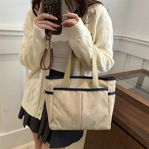 Beige corduroy tote bag with blue trim and shoulder straps shown on a model