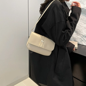 Borsa a tracolla beige minimalista con fibbia argento indossata su trench nero