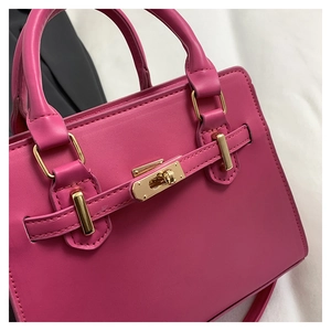Detail shot of a magenta leather handbag featuring a secure gold metallic twist lock