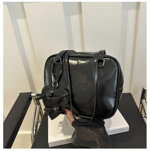Close-up of black patent leather shoulder bag with a heart pendant and bow detail