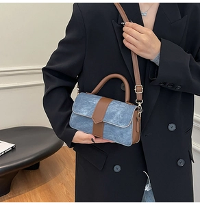 Detail of blue denim fabric and brown leather patchwork on a structured crossbody bag