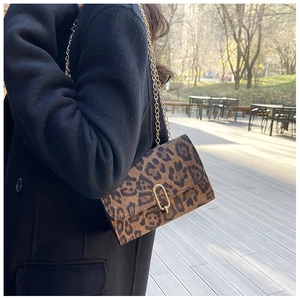 Détail du sac bandoulière léopard avec chaîne dorée porté par un mannequin en extérieur
