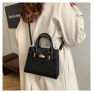 Detail of minimalist black leather handbag featuring gold metal clasp and belt strap design