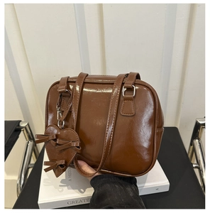 Detail of glossy brown faux leather shoulder bag with a heart charm and ribbon decor