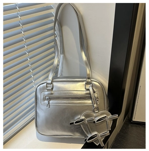 Detail of silver metallic shoulder bag featuring a front zipper and heart bow charm