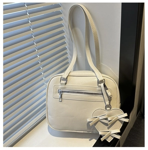 Detail of a beige leather shoulder bag with heart charm and bow on shutter background