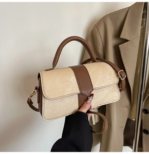 Detail of minimalist cream square handbag with brown leather trim and top handle held by hand