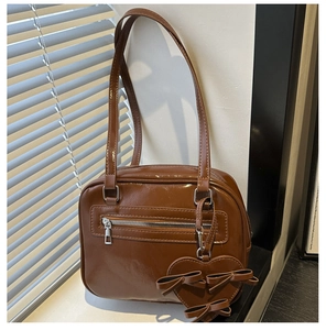 Detail of dark brown glossy PU leather handbag with heart charm and bow accessory