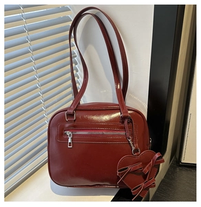Detail of burgundy glossy leather shoulder bag with chic heart charm and zipper pocket