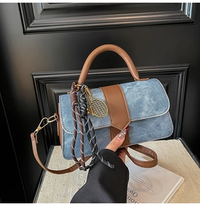 Detail of blue denim handbag with brown leather trim and golden tennis racket charm