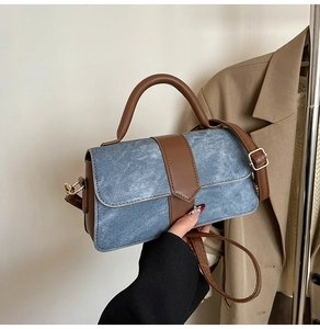 Detail of blue denim and brown leather stitching on a mini crossbody bag with gold hardware