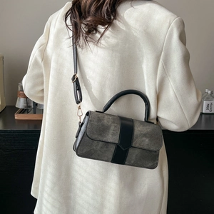 Minimalist grey suede crossbody bag with black leather trim worn by a model in a blazer