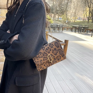 Sac bandoulière chic à imprimé léopard avec chaîne dorée porté sur un manteau noir