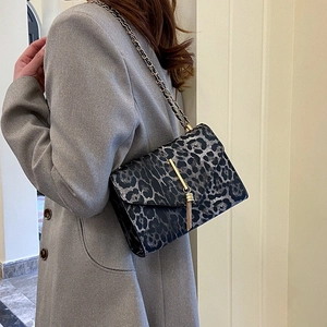 Umhängetasche mit Leopardenmuster, goldener Quaste und Kettenriemen auf grauem Blazer