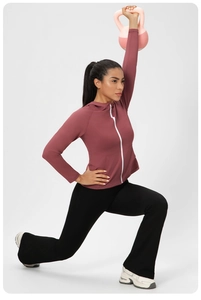 Femme en veste de yoga rose et legging évasé noir faisant des fentes avec un kettlebell
